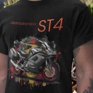 Puede incluir: Camiseta negra con un gráfico de motocicleta y el texto naranja "desmodromico ST4". La motocicleta es gris y roja con detalles amarillos, sobre un fondo de salpicaduras de pintura.