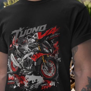 Op de afbeelding: Zwart T-shirt met een motorfietsafbeelding met rode en zwarte accenten. Het ontwerp bevat de tekst "TUONO V4 1100 FACTORY" en "1100cc UNLEASHED". De motorfietsafbeelding is gedetailleerd en gestileerd.