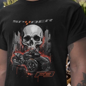 Könnte beinhalten: Schwarzes T-Shirt mit einer Grafik eines Schädels über einem schwarzen dreirädrigen Motorrad. Das Wort "SPYDER" steht über dem Schädel und "F3" unter dem Motorrad, alles in einer stilisierten Schriftart. Das Design hat rote Akzente.