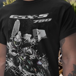 May include: Black t-shirt featuring a motorcycle graphic with the text "GSX-S 750" in white. The design includes a rider on a motorcycle in front of a city skyline. The shirt is made of a dark fabric.