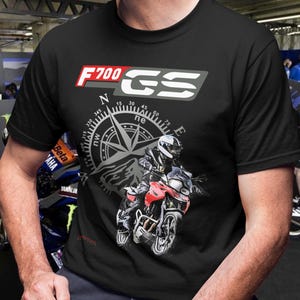 Peut inclure: T-shirt noir avec l'inscription "F700 GS" en rouge et gris, un motif de boussole et un dessin de moto rouge et noire. Le t-shirt est à col rond.