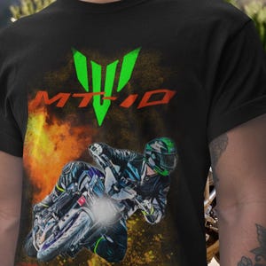 May include: Black t-shirt featuring a motorcycle racer in action, with a bright headlight and a fiery background. The shirt displays the text "MT-10" in red and a green logo.