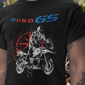 Pode incluir: Camiseta preta com um gráfico de motocicleta e um piloto. O design inclui o texto "R1150 GS" em azul e vermelho, e uma rosa dos ventos vermelha. A motocicleta é retratada em branco.