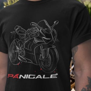 Può includere: T-shirt nera con un'illustrazione bianca di una moto. La parola "PANIGALE" è stampata in rosso e bianco. Il design include schizzi di vernice rossa. Una maglietta grafica per gli appassionati di moto.