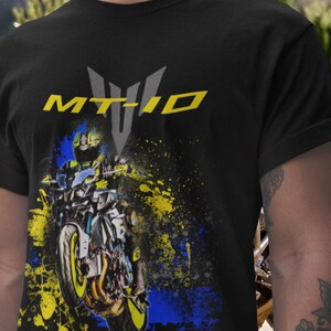 May include: Black t-shirt featuring a motorcycle graphic with yellow and blue paint splatter. The text "MT-10" is displayed in yellow and gray above the motorcycle image. The shirt is made of a soft material.
