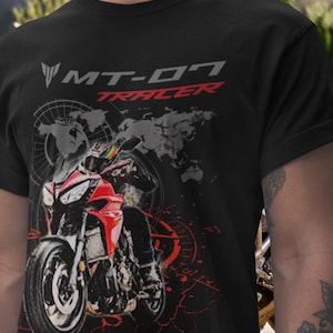 Pode incluir: Camiseta preta com um gráfico de motocicleta vermelha e preta. O texto "MT-07 Tracer" é exibido em branco e vermelho. O design inclui um mapa-múndi e uma bússola.