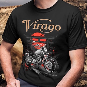 Puede incluir: Camiseta negra con un gráfico de motocicleta y la palabra "Virago". El diseño incluye un sol rojo y una puerta torii japonesa. La motocicleta está representada en tonos grises y blancos, con detalles en rojo.