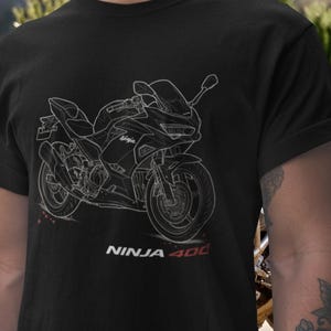 Op de afbeelding: Zwart T-shirt met een witte omtrek van een Ninja 400 motorfiets. De tekst "NINJA 400" is in wit en rood aan de onderkant gedrukt. Het motorfietsontwerp bevat details zoals de wielen, uitlaat en kuip.