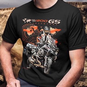 May include: Black t-shirt featuring a motorcycle graphic with the text "R1200 GS Adventure". The design includes a rider on a motorcycle, a world map, and compass elements. The shirt is made of a soft, comfortable material.