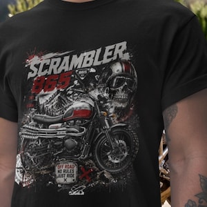 以下が含まれることがあります： 黒いTシャツ。バイクのグラフィックデザインで、「SCRAMBLER 865」の文字、スカル、ヘルメット、「OFF ROAD NO RULES JUST RIDE」の文字が含まれています。バイクは赤と黒です。
