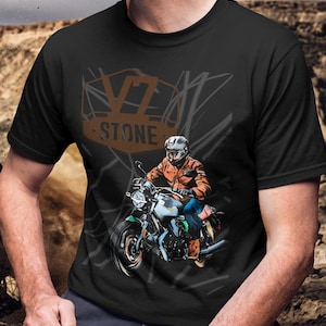 Könnte beinhalten: Schwarzes T-Shirt mit einer Motorradgrafik und einem Fahrer mit Helm und Jacke. Das Shirt zeigt den Text "VZ STONE" in Braun und Beige. Der Hintergrund zeigt eine Wüstenlandschaft.