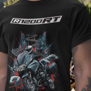 Pode incluir: Camiseta preta com um gráfico de motocicleta e o texto "R1200RT" em branco. O design inclui uma motocicleta azul, um piloto e ondas estilizadas com detalhes em vermelho. Roupa com tema de motocicleta.