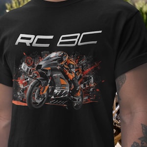 Könnte beinhalten: Ein schwarzes Kurzarm-T-Shirt mit einem Grafikdruck eines Motorradfahrers auf einer Sportmaschine. Das Design enthält den Text RC BC in weißer Schrift oben sowie orangefarbene und schwarze abstrakte mechanische Elemente um das Motorrad.