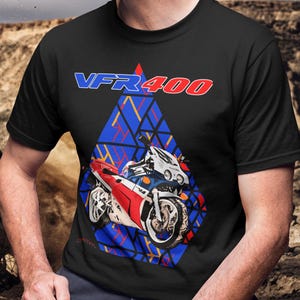 Könnte beinhalten: Schwarzes T-Shirt mit einem Motorrad-Grafik und dem Text "VFR 400" in Blau und Rot. Das Motorraddesign ist rot, weiß und blau, vor einem geometrischen blauen Hintergrund. Das T-Shirt hat einen Rundhalsausschnitt.