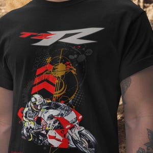 May include: Black t-shirt featuring a motorcycle graphic with a rider in a helmet. The design includes red and white accents, geometric shapes, and the text "TZR" in white and red. The shirt has a crew neck.