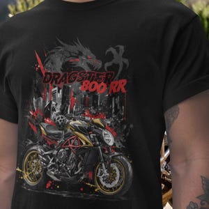 Pode incluir: Camiseta preta com um gráfico de motocicleta e o texto "DRAGSTER 800 RR". O design inclui um dragão, um horizonte urbano e toques de vermelho e amarelo. A motocicleta é preta, dourada e vermelha.