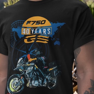 Puede incluir: Camiseta negra con un diseño de motocicleta y el texto "F750 40 YEARS GS". El diseño incluye un mapa del mundo azul, una brújula y un sol amarillo y azul.