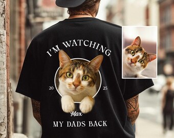 May include: Black t-shirt with a cat graphic inside a white circle, with the text "I'M WATCHING" above the cat and "MY DADS BACK" below. The cat is brown, white, and orange. The shirt also has the text "Max" and the numbers "20" and "25".