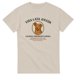 Könnte beinhalten: Beiges T-Shirt mit einer Illustration eines braunen Hundes in einem kreisförmigen Rahmen. Der Text "VIRA-LATA AMADA" steht darüber und "CACHAÇA PREMIUM CANINA" darunter. Weitere Texte geben den Firmennamen und den Standort an.