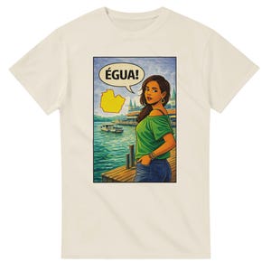 Puede incluir: Camiseta color crema con una ilustración estilo cómic. La obra de arte representa a una mujer con una blusa verde y vaqueros, con un bocadillo que dice "ÉGUA!". También se incluye un mapa amarillo en el bocadillo. El fondo muestra una escena frente al mar.