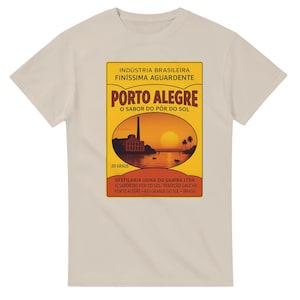 May include: A beige t-shirt featuring a vintage-style graphic. The graphic is a rectangular design with the words "PORTO ALEGRE" in large letters, and other text in Portuguese. The design includes a sunset scene with a building and palm trees.