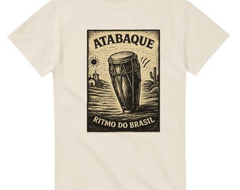 May include: Cream-colored t-shirt featuring a black and white illustration of an atabaque drum. The design includes the word "ATABAQUE" at the top and "RITMO DO BRASIL" at the bottom, with a desert landscape background.