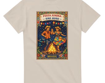 May include: Beige t-shirt featuring a colorful illustration of a couple dancing around a bonfire. The image includes the text "Festa Junina - São João" and "Brasil". The artwork depicts a festive scene with vibrant colors and a celebratory atmosphere.