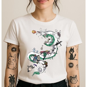 May include: White t-shirt featuring a detailed illustration of a dragon with green and white accents, and several animated characters. The design includes a variety of colors and is printed on a white, short-sleeved shirt.