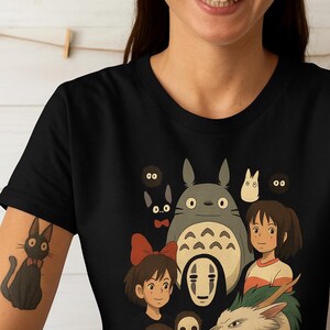 May include: Black t-shirt featuring a colorful graphic of characters from a popular animated film. The design includes a large gray creature with a white belly, a girl with a red bow, and other animated figures. The shirt is made of a soft material.