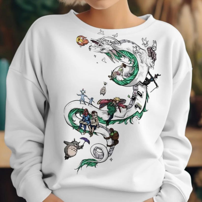 May include: White sweatshirt featuring a detailed illustration of a white dragon with green accents, and various cartoon characters. The design includes a variety of characters and elements, creating a whimsical and artistic aesthetic.