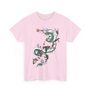 May include: A light pink t-shirt featuring a detailed illustration of a white and green dragon with various animated characters. The design includes characters from popular animated films, creating a whimsical and artistic aesthetic.