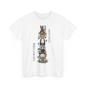 Puede incluir: Camiseta blanca con una ilustraci&oacute;n apilada de personajes de Studio Ghibli. El dise&ntilde;o incluye personajes como Totoro, Sin Rostro y otros, con texto japon&eacute;s y "STUDIO GHIBLI" impreso verticalmente.