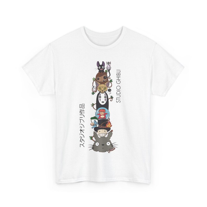 Puede incluir: Camiseta blanca con una ilustraci&oacute;n apilada de personajes de Studio Ghibli. El dise&ntilde;o incluye personajes como Totoro, Sin Rostro y otros, con texto japon&eacute;s y "STUDIO GHIBLI" impreso verticalmente.