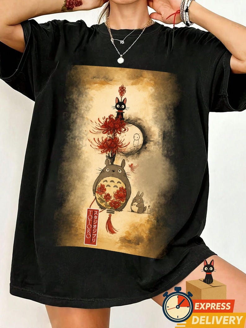 May include: Black t-shirt with a colourful illustration from the animated film "My Neighbour Totoro." The design includes Totoro, a black cat, a rabbit, and red flowers. The Japanese text "Totoro" is visible on a lantern.