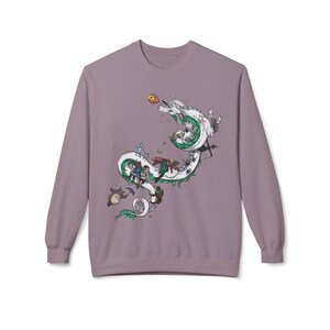 May include: A mauve long-sleeve sweatshirt featuring a detailed graphic of a white dragon with green accents, carrying various animated characters. The design includes a variety of colorful figures and objects, creating a whimsical and detailed scene.
