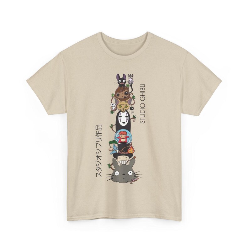 Puede incluir: Camiseta beige con una pila vertical de personajes de Studio Ghibli. El dise&ntilde;o incluye personajes como Totoro y Sin Rostro, con texto japon&eacute;s y "STUDIO GHIBLI" impreso verticalmente en el lado derecho.