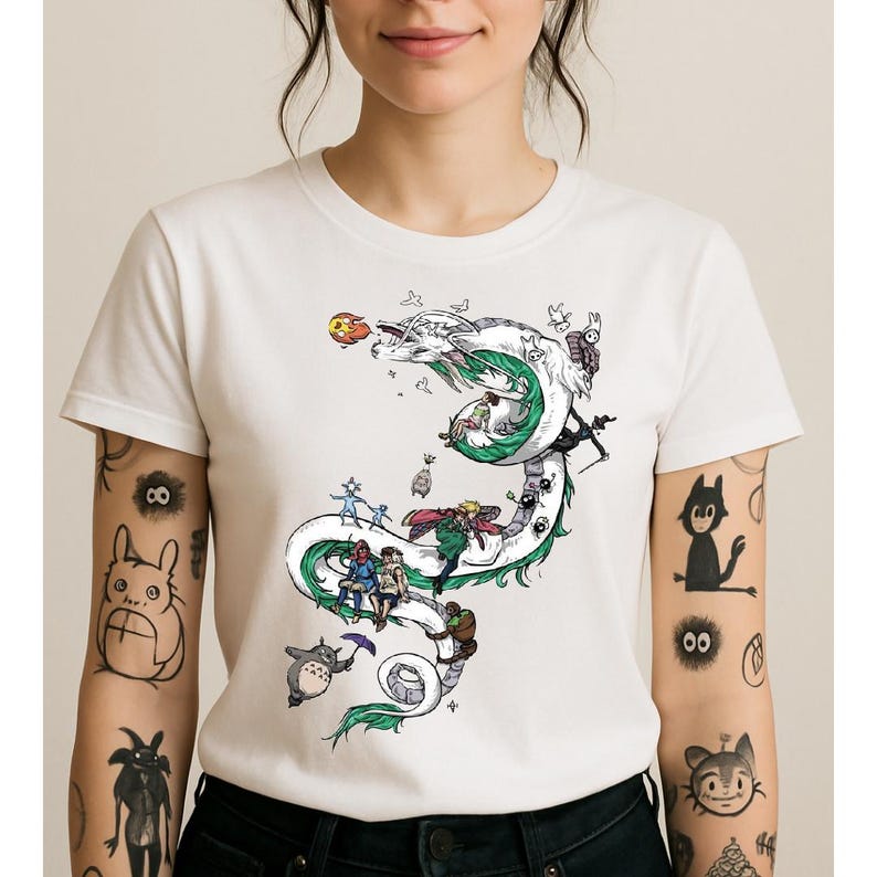 May include: White t-shirt featuring a detailed illustration of a dragon with green and white accents, and several animated characters. The design includes a variety of colors and is printed on a white, short-sleeved shirt.
