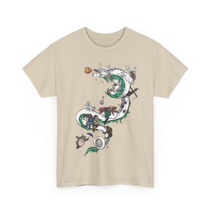 May include: Beige t-shirt featuring a detailed illustration of a white and green dragon with various animated characters. The dragon winds across the shirt, with characters riding on its back. The design includes a variety of colors and intricate details.