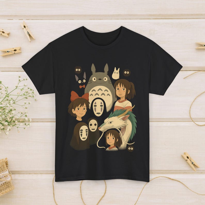 May include: Black t-shirt with a vibrant graphic of characters from the animated films Spirited Away and My Neighbor Totoro. The design includes Totoro, Chihiro, No-Face, and Haku. The shirt is made of a soft material.
