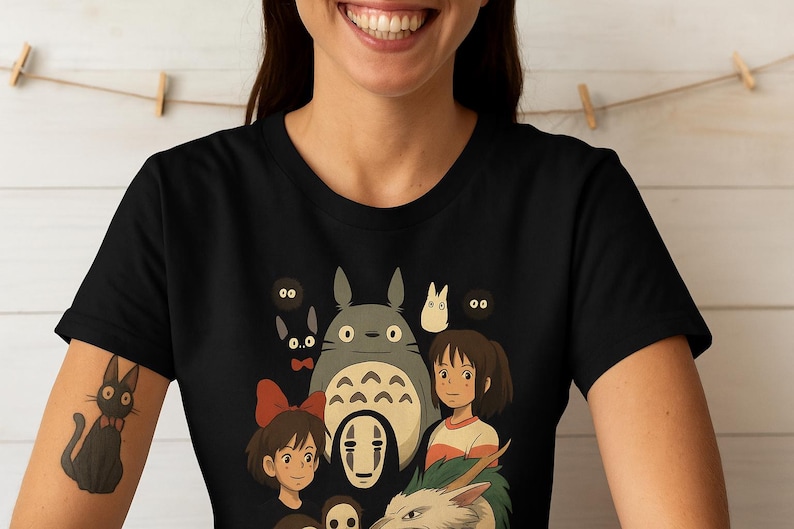 May include: Black t-shirt with a vibrant graphic of animated characters. The design includes a large grey creature, a girl with a red bow, and other figures. The shirt is made of a soft material. A popular animated film theme.