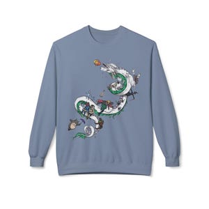 May include: A light blue sweatshirt featuring a whimsical illustration of a white dragon with green accents, adorned with various animated characters. The design includes a variety of colorful figures and objects, creating a playful and imaginative scene.