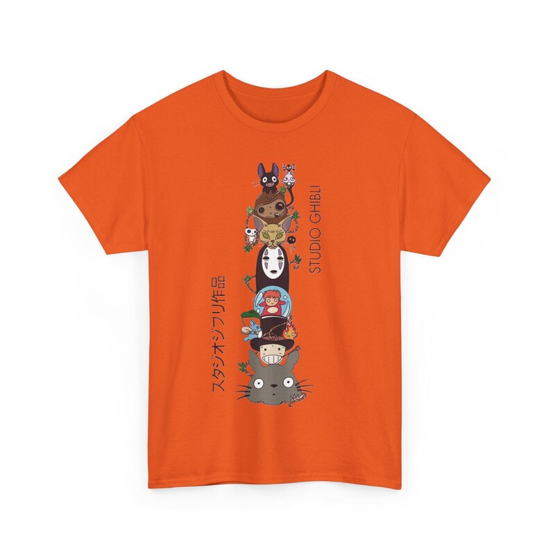 Puede incluir: Camiseta naranja con un dise&ntilde;o apilado de dibujos animados de personajes de Studio Ghibli, incluyendo a Totoro y Sin Rostro. Texto japon&eacute;s impreso verticalmente a la izquierda, con "STUDIO GHIBLI" a la derecha. Un dise&ntilde;o vibrante y colorido en una camiseta cl&aacute;sica.