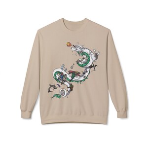 May include: Beige long-sleeve sweatshirt featuring a detailed illustration of a white dragon with green accents, carrying various animated characters. The design includes a mix of colors and cartoon elements, creating a whimsical aesthetic.