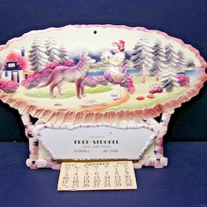 May include: Vintage 1932 calendar featuring a painted scene of Little Red Riding Hood and the wolf in a forest setting. The calendar includes the month of January and the name "Fred Strobel". The calendar is made of paper and cardboard.