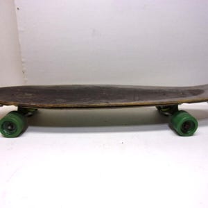 May include: A vintage skateboard with a dark brown deck and green wheels. The skateboard has a classic design, with a slightly curved shape and a worn appearance, suggesting it has been used. The green wheels provide a pop of color against the darker deck.