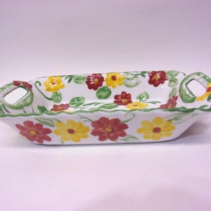 May include: A rectangular ceramic serving dish with a white base, adorned with a floral pattern of yellow and red flowers and green leaves. The dish has two handles and a green trim. Ideal for serving snacks or appetizers.