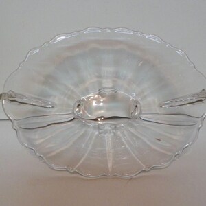 May include: Clear glass serving dish with a scalloped edge and three sections. The dish has a central handle and two side handles. The design features a radial pattern emanating from the center.