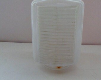 May include: A vintage, white glass light fixture with a rectangular shape and a textured, ribbed design on the front. The fixture has a rounded bottom and a slightly angled top. A small spot of rust is visible on the bottom.