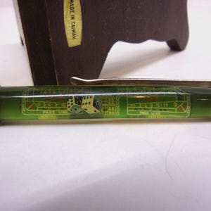 May include: A vintage pen with a green barrel featuring a casino-themed design, including dice and a craps table layout. The pen has a silver clip and black accents. The pen is set against a blurred background.