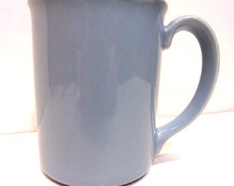 May include: A solid, light blue ceramic mug with a curved handle. The mug has a simple, classic design and a glossy finish. The mug is suitable for hot or cold beverages.